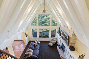 Living area with beamed ceiling, a glass covered fireplace, high vaulted ceiling, dark wood-style flooring, and a ceiling fan