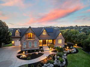 View of front of home featuring a porch, stone siding, curved driveway, roof mounted solar panels, and a garage