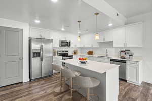 Kitchen with appliances with stainless steel finishes, white cabinetry, a breakfast bar, a kitchen island, and dark wood-style flooring