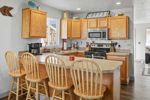 Kitchen with appliances with stainless steel finishes, light countertops, a breakfast bar area, dark wood-style floors, and recessed lighting