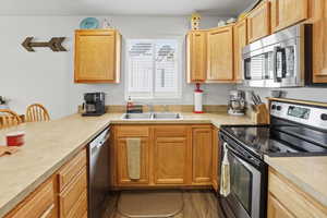 Kitchen with stainless steel appliances, light countertops, a bar, and wood finished floors