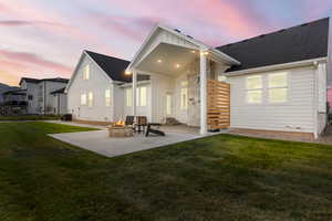 Back of house at dusk featuring a patio, a lawn, board and batten siding, a fire pit, and a shingled roof