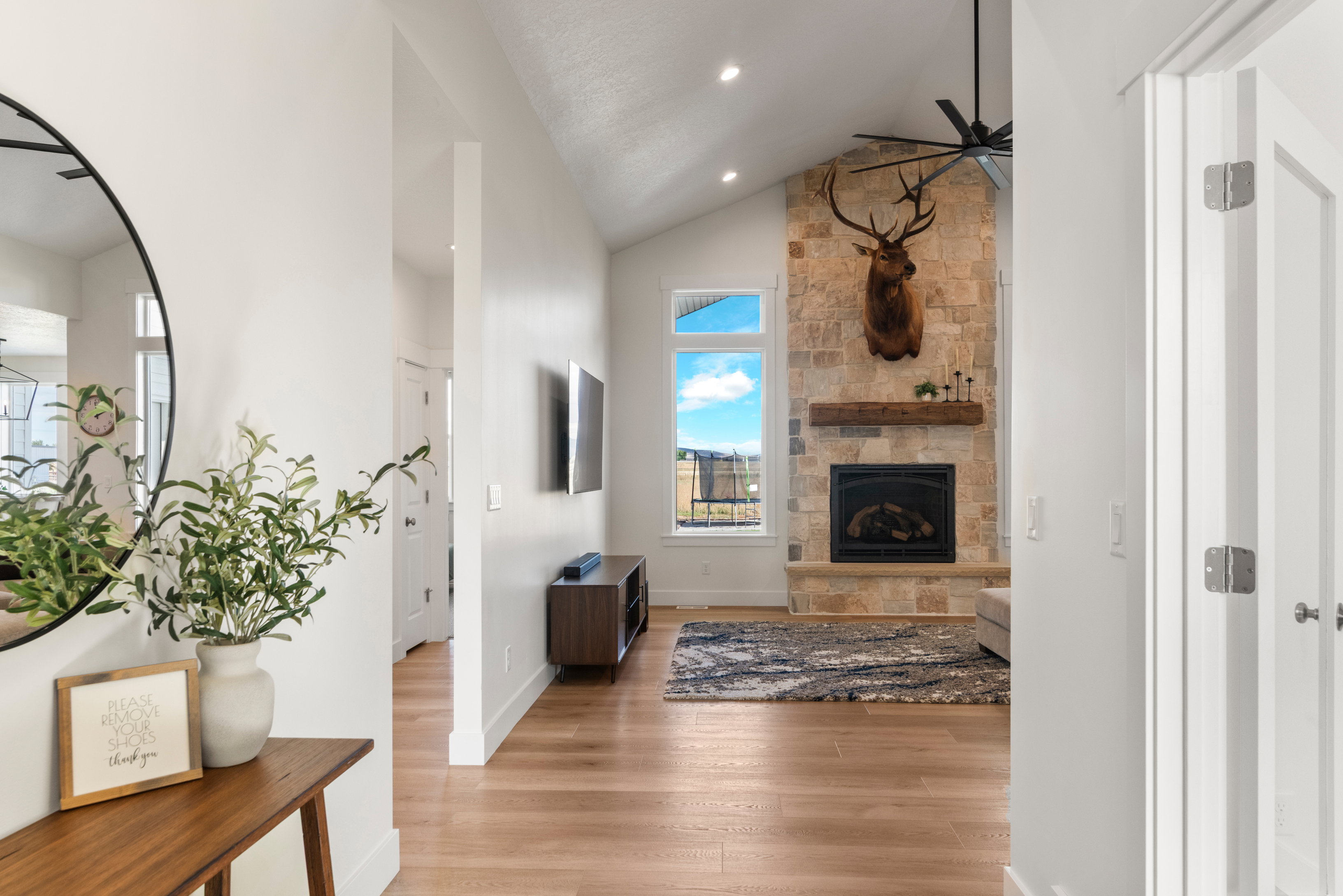 Living area featuring high vaulted ceiling, a stone fireplace, light wood-style flooring, a ceiling fan, and recessed lighting
