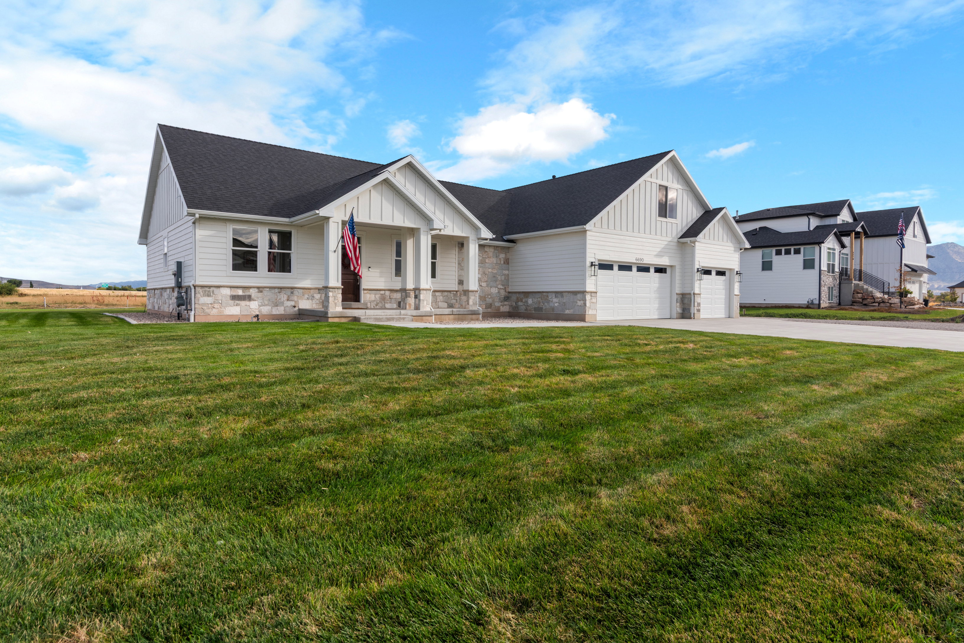 Modern inspired farmhouse with board and batten siding, a porch, stone siding, a front lawn, and driveway