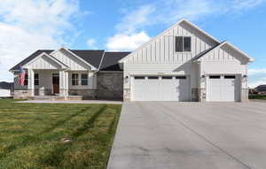 Modern farmhouse featuring board and batten siding, a porch, a front yard, concrete driveway, and stone siding