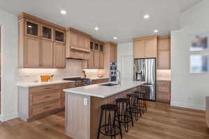 Kitchen featuring stainless steel appliances, an island with sink, light wood finished floors, light brown cabinetry, and recessed lighting