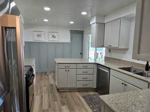 Kitchen with a peninsula, light wood-style floors, light stone counters, a decorative wall, and recessed lighting