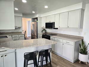 Kitchen with light wood-style floors, appliances with stainless steel finishes, a peninsula, recessed lighting, and light stone countertops