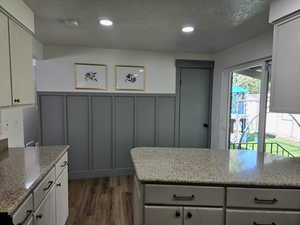 Kitchen featuring dark wood-style flooring, light stone countertops, a textured ceiling, a decorative wall, and recessed lighting