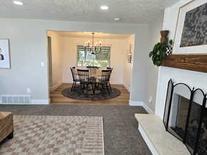 Dining area featuring a fireplace with raised hearth, a textured ceiling, a chandelier, dark colored carpet, and recessed lighting