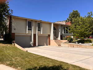 Split foyer home featuring concrete driveway, a garage, and a chimney