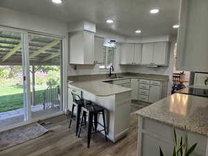 Kitchen featuring recessed lighting, dark wood-style floors, a textured ceiling, a peninsula, and light stone countertops