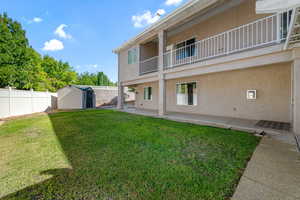 Fenced backyard featuring a storage unit, a balcony, and a patio