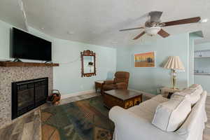 Living room with a textured ceiling, a tile fireplace, wood finished floors, and ceiling fan