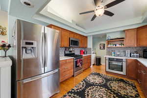 Kitchen with stainless steel appliances, a tray ceiling, brown cabinetry, light wood-style floors, and a textured ceiling