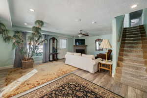 Living room featuring a textured ceiling, a fireplace, wood finished floors, stairs, and a ceiling fan