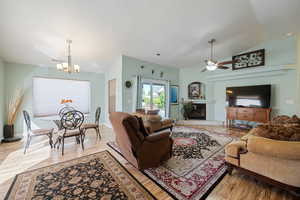 Living area with lofted ceiling, a glass covered fireplace, light wood-style floors, ceiling fan, and a textured ceiling