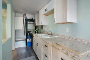 Kitchen featuring dark wood finished floors, white cabinetry, light countertops, and a textured wall