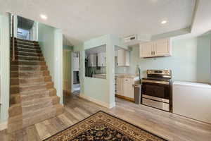 Kitchen featuring electric stove, a textured ceiling, recessed lighting, light wood-type flooring, and light stone counters