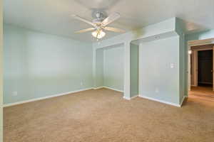 Carpeted empty room featuring ceiling fan and a textured ceiling