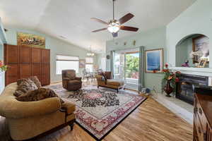 Living room with a fireplace, light wood-type flooring, a chandelier, a textured ceiling, and lofted ceiling