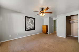 Unfurnished bedroom featuring a textured ceiling, a closet, light colored carpet, and a ceiling fan