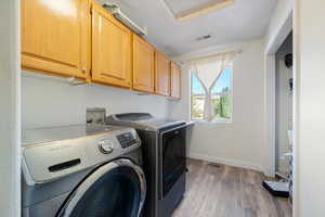 Washroom with light wood-style floors, cabinet space, and washing machine and dryer