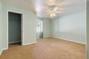 Unfurnished bedroom featuring a textured ceiling, light carpet, a walk in closet, and a ceiling fan