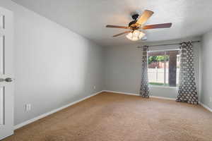 Carpeted empty room with a textured ceiling and ceiling fan