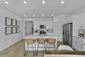 Kitchen featuring stainless steel appliances, recessed lighting, white cabinetry, light wood-type flooring, and a breakfast bar