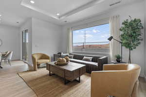 Living room featuring light wood-style flooring, a tray ceiling, and recessed lighting