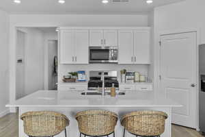 Kitchen with light wood-style floors, white cabinetry, recessed lighting, appliances with stainless steel finishes, and a kitchen bar