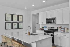 Kitchen with stainless steel appliances, white cabinets, a breakfast bar area, and recessed lighting