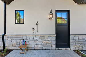 Entrance to property with stone siding, stucco siding, and a patio