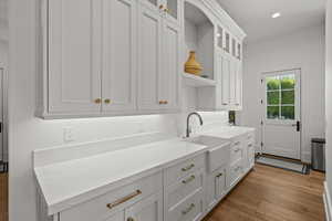 Kitchen featuring glass insert cabinets, white cabinets, light wood-style flooring, light stone countertops, and recessed lighting