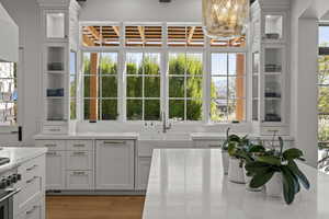 Kitchen featuring glass insert cabinets, white cabinets, light wood-style floors, and light stone counters