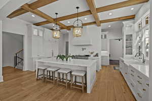 Kitchen with glass insert cabinets, white cabinetry, a kitchen bar, a large island with sink, and coffered ceiling