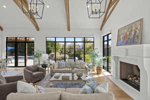 Living area featuring a chandelier, high vaulted ceiling, wood finished floors, a fireplace with raised hearth, and beam ceiling