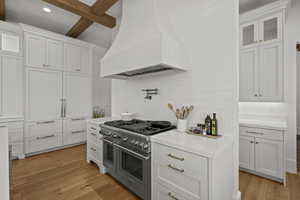 Kitchen featuring range with two ovens, white cabinets, custom exhaust hood, light wood finished floors, and glass insert cabinets