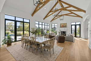 Dining room featuring high vaulted ceiling, a fireplace, beamed ceiling, light wood-style flooring, and a chandelier