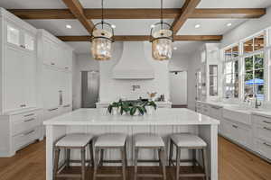 Kitchen with glass insert cabinets, a breakfast bar area, a large island, beam ceiling, and light wood-type flooring