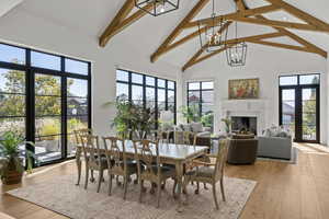Dining room with high vaulted ceiling, a fireplace, light wood-style flooring, beamed ceiling, and a chandelier