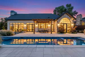 Back of house at dusk with a patio, a chimney, stone siding, a shingled roof, and a pergola