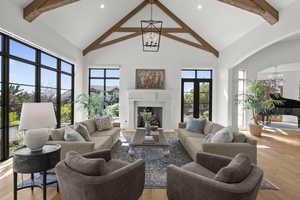 Living room with a chandelier, high vaulted ceiling, beam ceiling, light wood-style flooring, and a fireplace