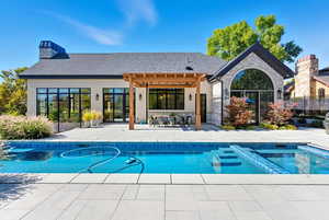 Rear view of house with a patio, roof with shingles, a pergola, stone siding, and a chimney