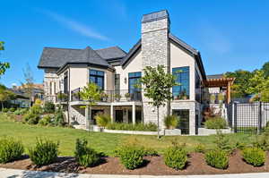 Back of house with stone siding, stucco siding, and a shingled roof