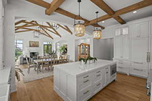 Kitchen with white cabinets, pendant lighting, beamed ceiling, light wood-style floors, and open floor plan