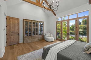 Bedroom featuring high vaulted ceiling, beam ceiling, light wood finished floors, access to exterior, and a chandelier
