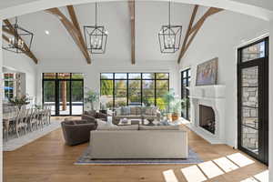 Living area with high vaulted ceiling, light wood-type flooring, a fireplace with raised hearth, recessed lighting, and beamed ceiling