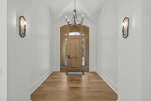 Foyer entrance featuring a chandelier, light wood-type flooring, and lofted ceiling